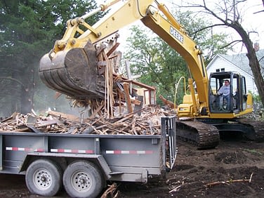 An excavator removing debris onto a flatbed trailer.