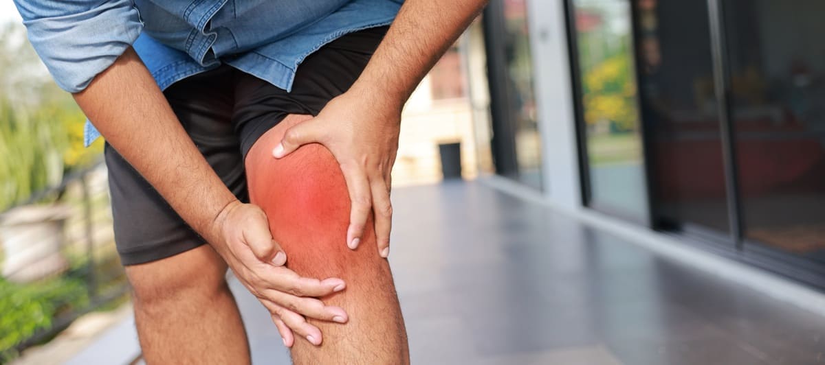 Close-up of hand holding painful injured knee with red inflamed spot and bruising Medical concept of joint pain arthritis bone injury muscle ache or sprain in outdoor sunlight background | Walker Road Chiropractic Injured knee bursitis