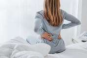 Woman with back ache Young woman with back ache, she is sitting on the bed and touching her back