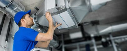 technician in  Reno, NV fixing hvac system in a blue shirt and hat