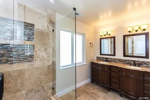 3b-480w | Advance Installations Bathroom with glass-enclosed walk-in shower on left, beige tile walls and floor, and a dark wood double vanity with three mirrors and warm light fixtures.