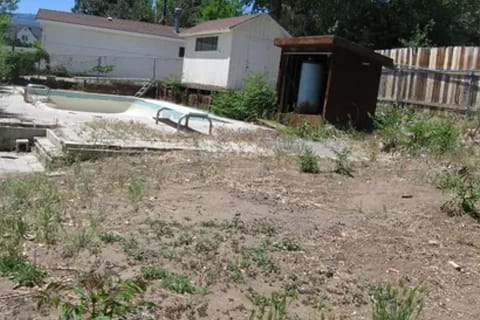 gallery10-b | Advance Installations Backyard with an empty, dilapidated in-ground pool, overgrown weeds, and a small brown shed near a wooden fence.