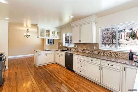 gallery2-a | Advance Installations Bright kitchen with white cabinets, granite countertops, stainless steel dishwasher, and large windows along the counter; warm hardwood floors.