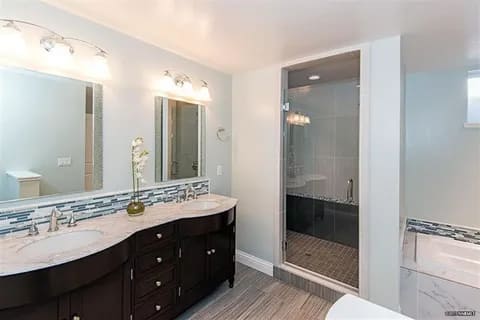 gallery5-a | Advance Installations Double-sink bathroom vanity with dark wood cabinets, marble countertop, two mirrors, and a glass-walled shower.