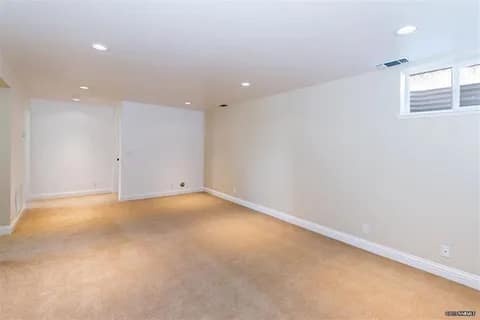 gallery6-a | Advance Installations Empty beige-carpeted basement with white walls, recessed ceiling lights, and a small high window at the far end.