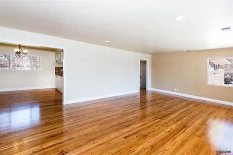gallery8-a | Advance Installations Empty living room with polished hardwood floors, light beige walls, white baseboards, and recessed lighting across the ceiling.
