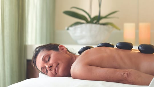 OC Aquamara Spa | Holiday Planit Woman lying face down, receiving a hot stone massage on her back in a spa setting.